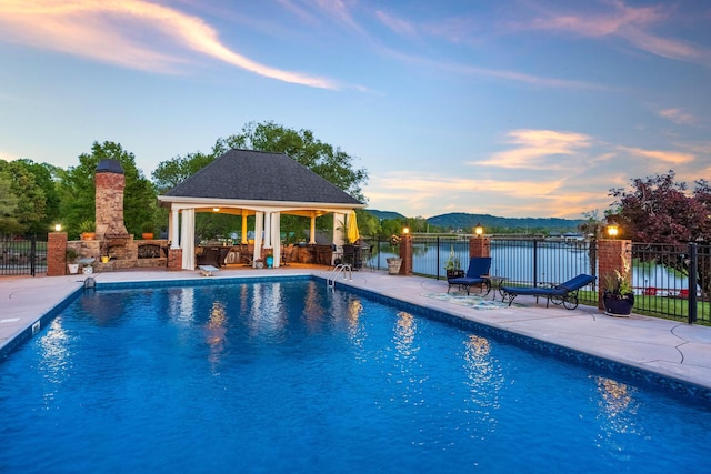 pool at dusk featuring a water view, a patio area, and a gazebo