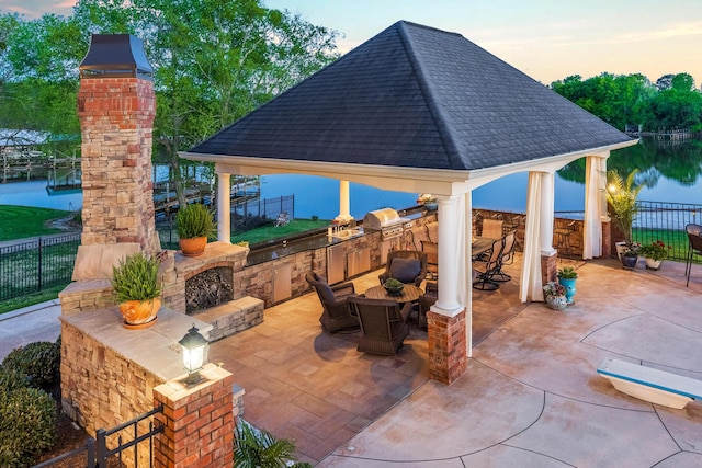 patio terrace at dusk featuring a water view, area for grilling, a grill, and a gazebo