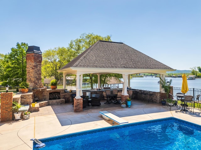 view of swimming pool featuring a water view, a patio area, an outdoor stone fireplace, and a gazebo