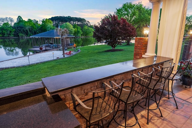 exterior space featuring an outdoor bar, a water view, a dock, and a lawn