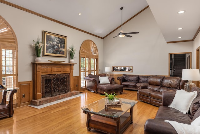 living room with a fireplace, light wood-type flooring, high vaulted ceiling, ornamental molding, and ceiling fan