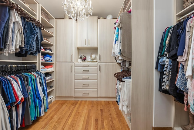 walk in closet with light hardwood / wood-style flooring and an inviting chandelier