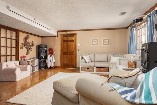 living room featuring a textured ceiling, ornamental molding, and light wood-type flooring