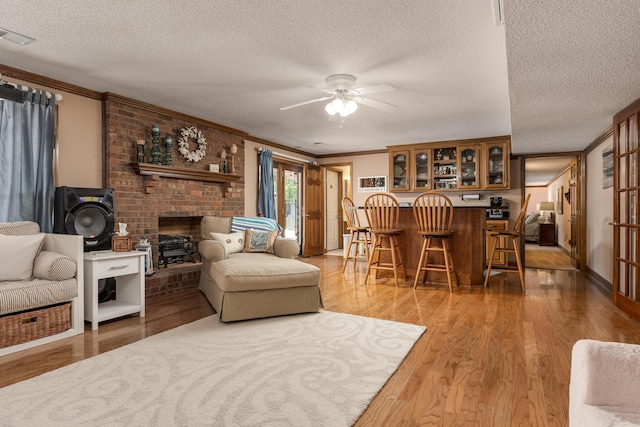 living room featuring a fireplace, crown molding, a textured ceiling, ceiling fan, and light hardwood / wood-style floors