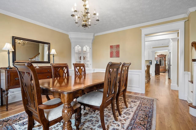 dining space featuring an inviting chandelier, crown molding, a textured ceiling, and light hardwood / wood-style flooring