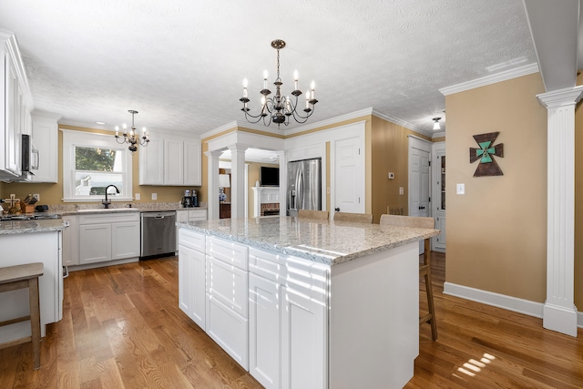 kitchen featuring a center island, decorative columns, stainless steel appliances, and light hardwood / wood-style flooring