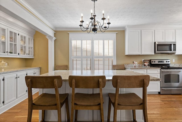 kitchen featuring a notable chandelier, a center island, stainless steel appliances, ornamental molding, and white cabinets