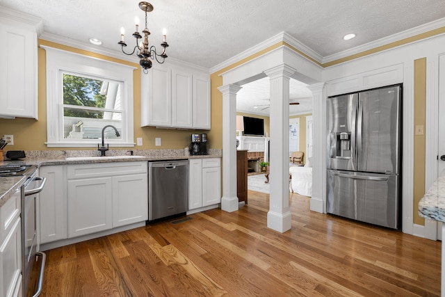 kitchen with light wood-type flooring, white cabinetry, stainless steel appliances, sink, and ornate columns