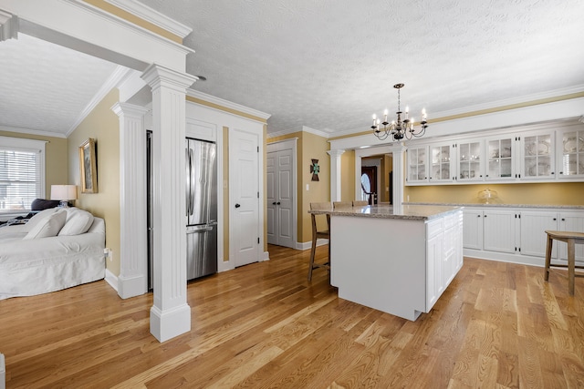 kitchen featuring a breakfast bar area, ornate columns, stainless steel refrigerator, white cabinetry, and light wood-type flooring