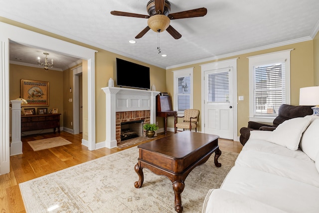 living room with light wood-type flooring, ceiling fan, a fireplace, and ornamental molding