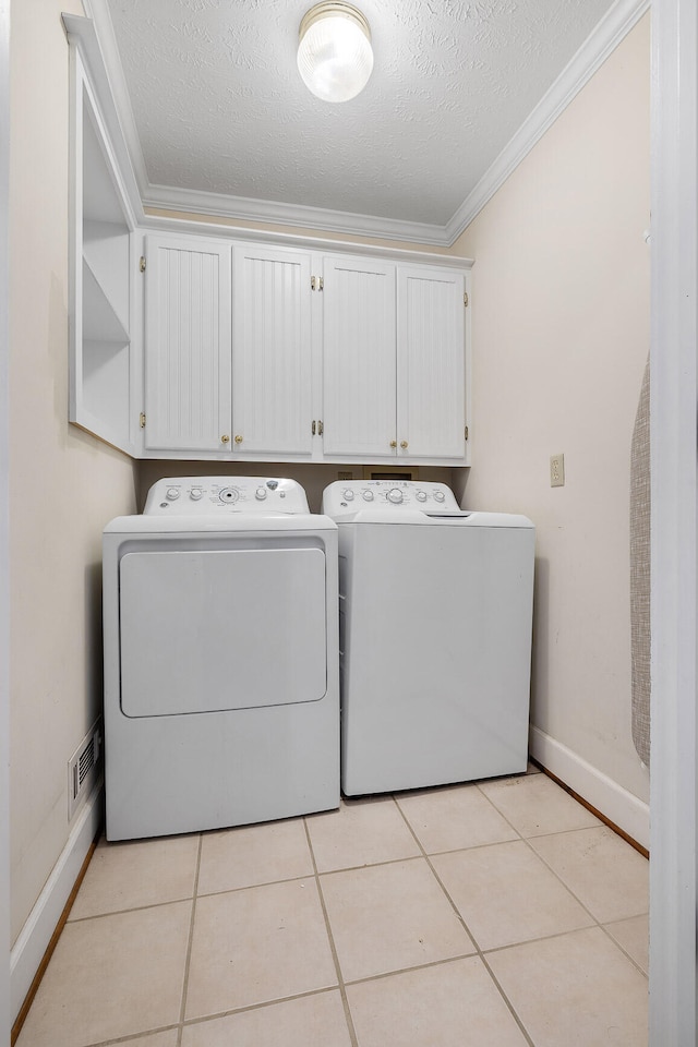 clothes washing area with washer and clothes dryer, light tile patterned floors, a textured ceiling, cabinets, and ornamental molding