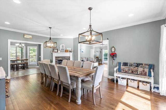 dining room featuring crown molding, a stone fireplace, a chandelier, and hardwood / wood-style flooring