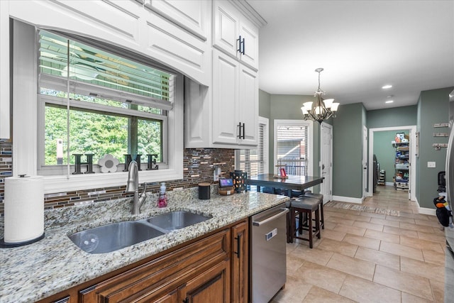 kitchen featuring white cabinets, hanging light fixtures, dishwasher, backsplash, and light stone countertops