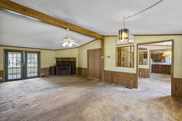 unfurnished living room with ceiling fan, a fireplace, wood walls, vaulted ceiling with beams, and carpet flooring