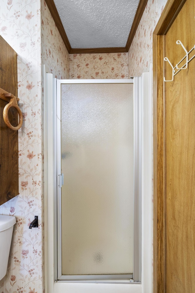 bathroom featuring crown molding, a textured ceiling, toilet, a stall shower, and wallpapered walls