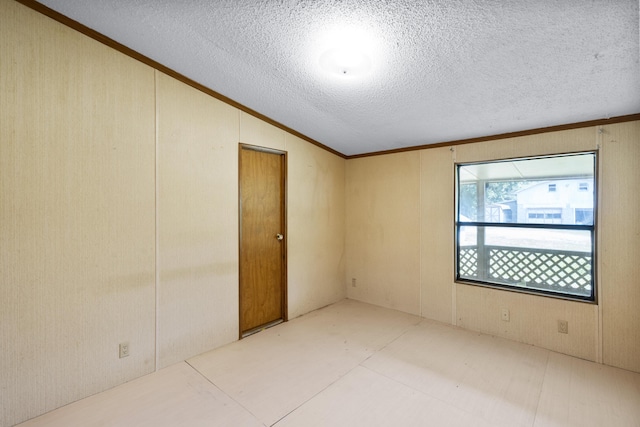 spare room with wood walls, vaulted ceiling, ornamental molding, and a textured ceiling