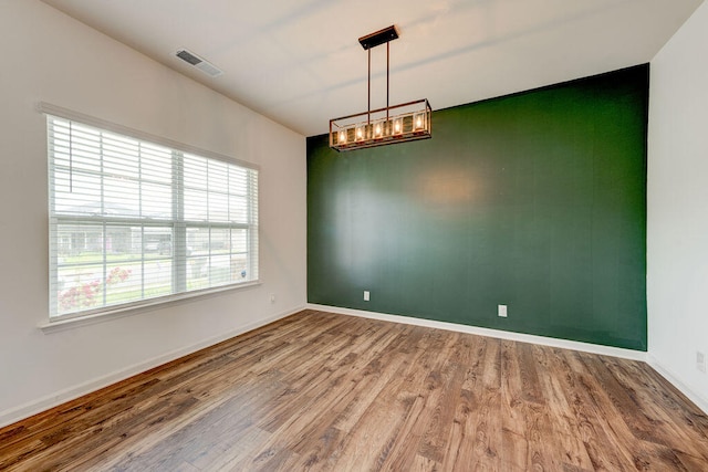 spare room with hardwood / wood-style flooring and an inviting chandelier