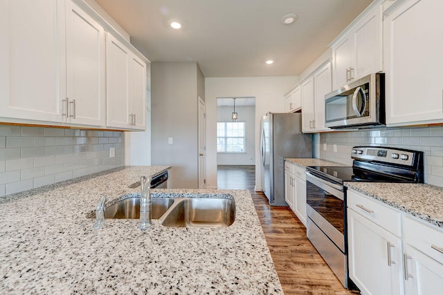 kitchen with tasteful backsplash, stainless steel appliances, light stone countertops, white cabinets, and light hardwood / wood-style floors