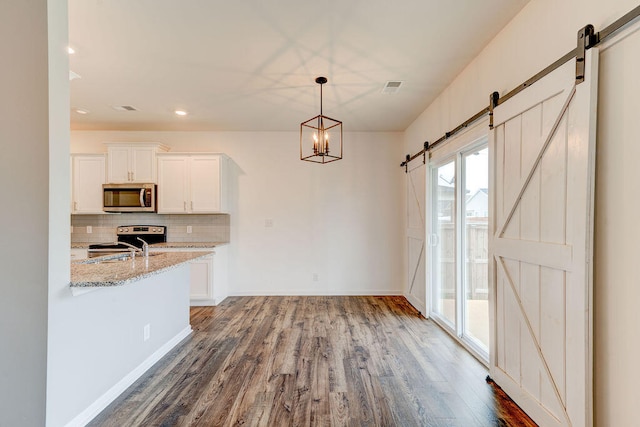 kitchen with stainless steel appliances, a barn door, light stone counters, hardwood / wood-style flooring, and white cabinets