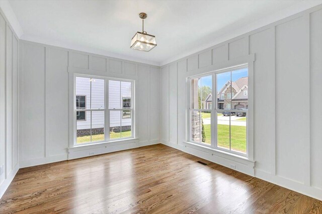 unfurnished dining area featuring visible vents, wood finished floors, and a decorative wall