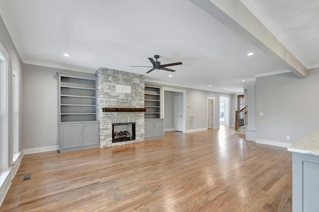 unfurnished living room with crown molding, built in shelves, light hardwood / wood-style floors, a stone fireplace, and ceiling fan