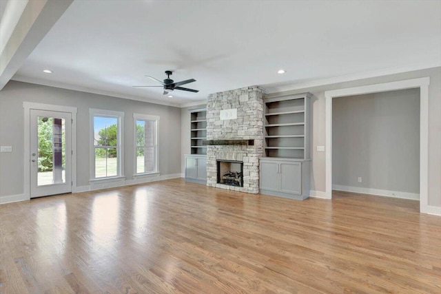 unfurnished living room featuring a fireplace, light hardwood / wood-style flooring, built in shelves, crown molding, and ceiling fan