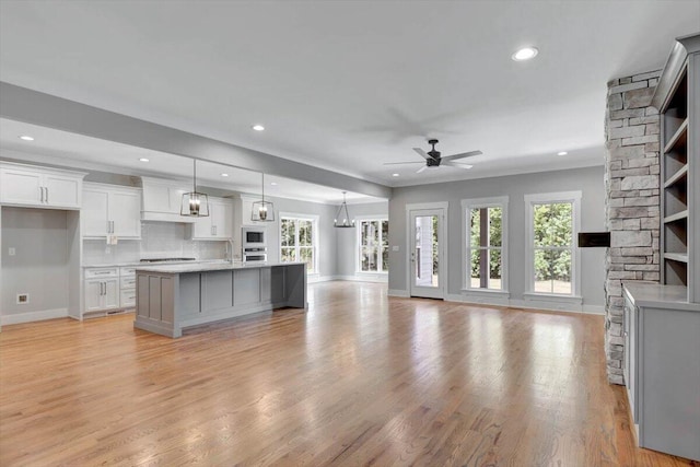 kitchen with hanging light fixtures, white microwave, light hardwood / wood-style flooring, ceiling fan, and a kitchen island with sink