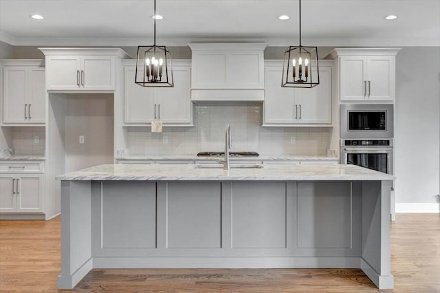 kitchen featuring light stone counters, light wood-type flooring, and a kitchen island with sink