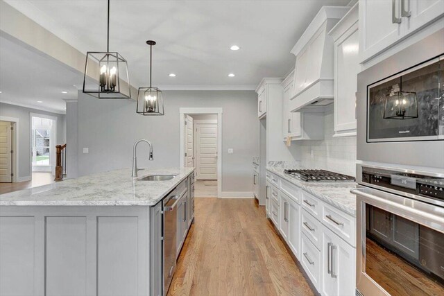 kitchen with a kitchen island with sink, stainless steel appliances, sink, light stone counters, and white cabinets