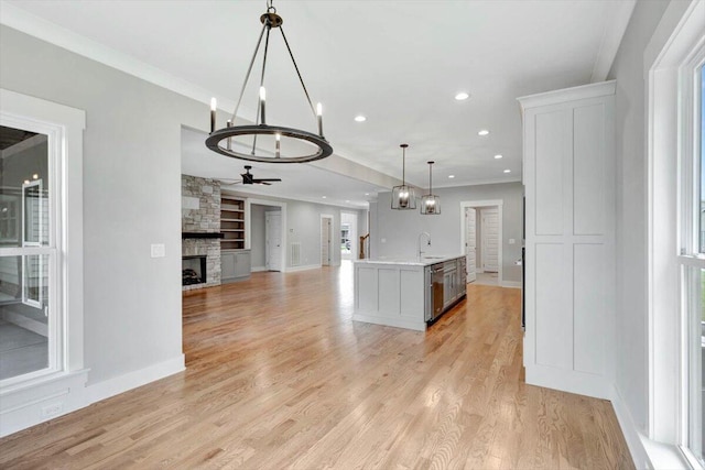 kitchen featuring a fireplace, an island with sink, ceiling fan, hanging light fixtures, and light hardwood / wood-style floors