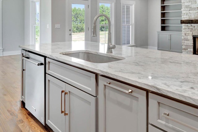 kitchen featuring dishwasher, light hardwood / wood-style flooring, light stone counters, sink, and a stone fireplace