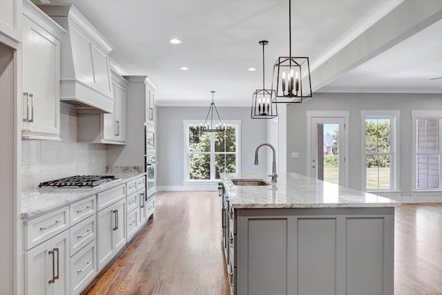 kitchen featuring light wood-type flooring, decorative light fixtures, light stone countertops, stainless steel appliances, and a center island with sink