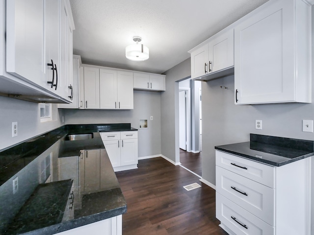 kitchen with a textured ceiling, dark stone countertops, dark hardwood / wood-style floors, and white cabinets