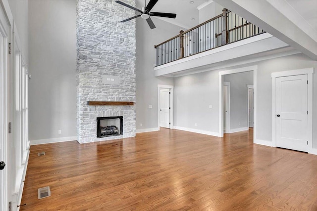 unfurnished living room featuring hardwood / wood-style floors, ceiling fan, and a stone fireplace