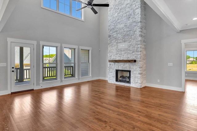 unfurnished living room with high vaulted ceiling, ceiling fan, hardwood / wood-style flooring, and a stone fireplace