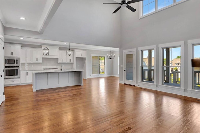 unfurnished living room featuring plenty of natural light, a high ceiling, ceiling fan with notable chandelier, and light wood-type flooring