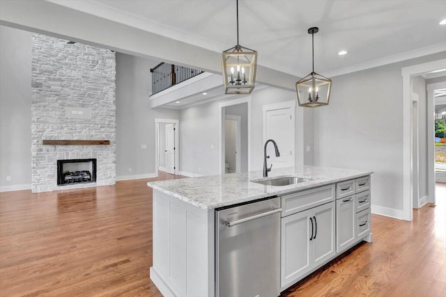 kitchen with dishwasher, an island with sink, sink, a stone fireplace, and light hardwood / wood-style floors