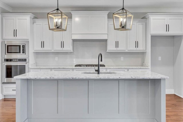 kitchen with a notable chandelier, appliances with stainless steel finishes, wood finished floors, and a kitchen island with sink