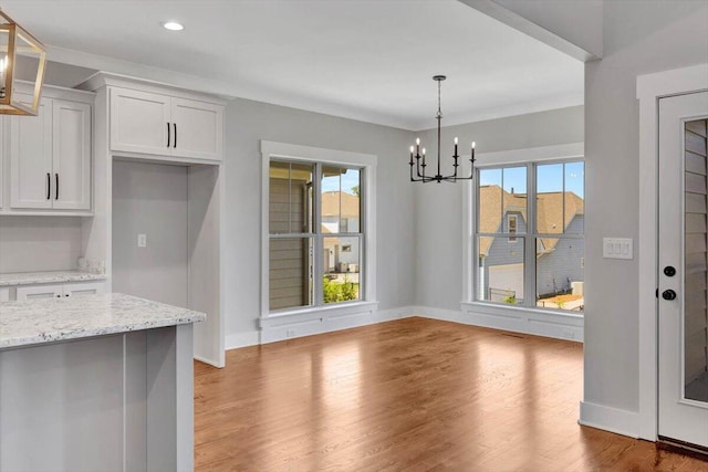 unfurnished dining area with a chandelier, plenty of natural light, and wood-type flooring