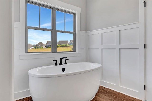 bathroom featuring a soaking tub, wainscoting, a decorative wall, and wood finished floors