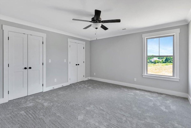 unfurnished bedroom with carpet flooring, two closets, ceiling fan, and crown molding