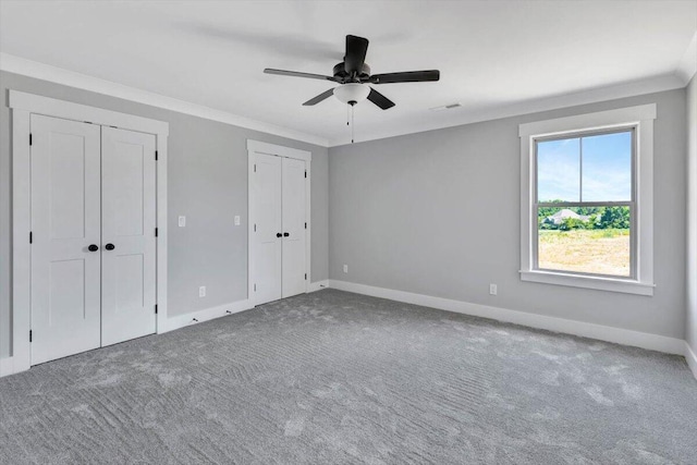 unfurnished bedroom featuring visible vents, multiple closets, carpet floors, and crown molding