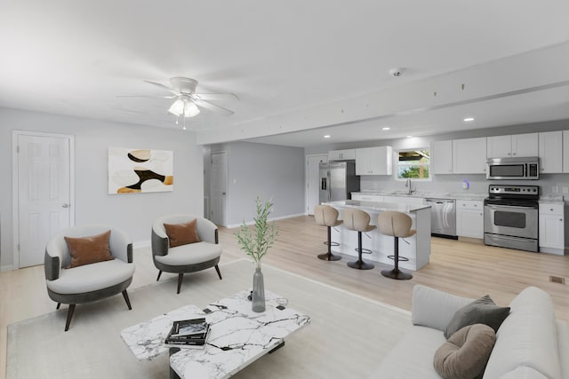 living room with light hardwood / wood-style floors, ceiling fan, and sink