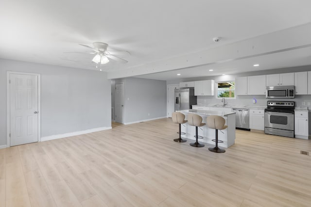 kitchen with appliances with stainless steel finishes, light hardwood / wood-style floors, a kitchen island, a kitchen bar, and ceiling fan