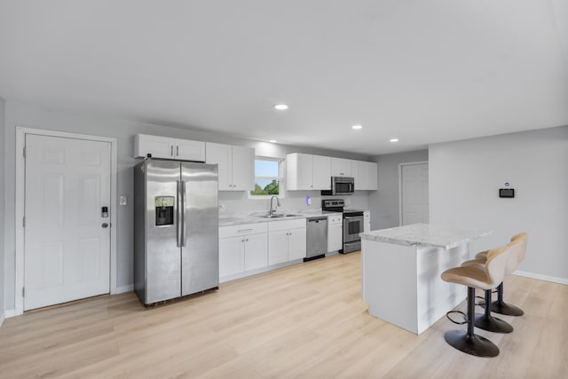 kitchen featuring appliances with stainless steel finishes, white cabinets, light wood-type flooring, a center island, and sink