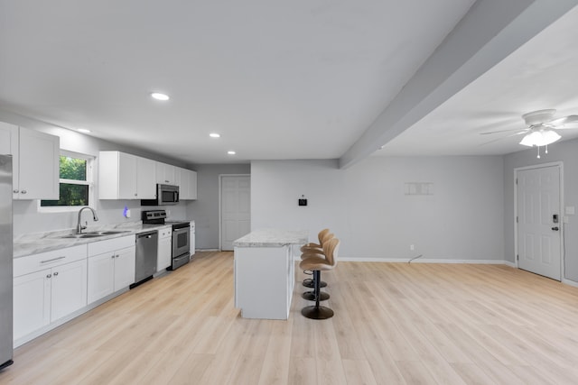 kitchen with light stone counters, appliances with stainless steel finishes, light wood-type flooring, and white cabinetry