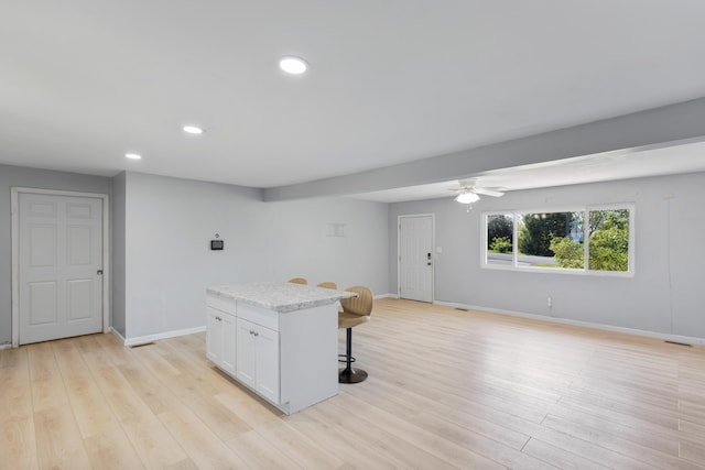 kitchen featuring ceiling fan, light hardwood / wood-style flooring, white cabinetry, a center island, and a breakfast bar area