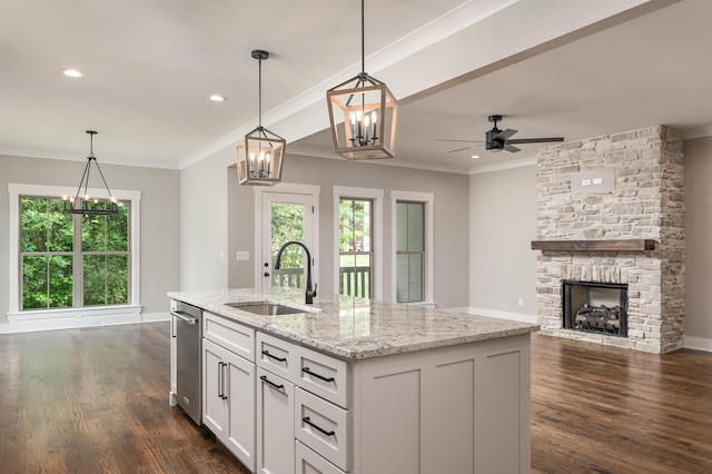 kitchen featuring a fireplace, ceiling fan with notable chandelier, an island with sink, sink, and dark hardwood / wood-style floors