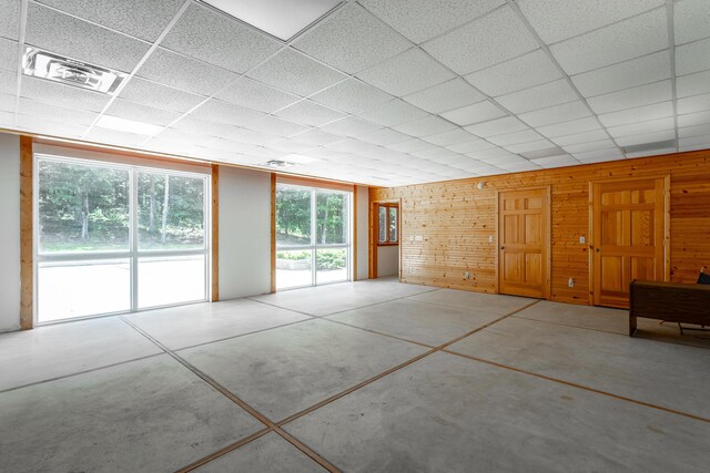 unfurnished room featuring wood walls and a drop ceiling