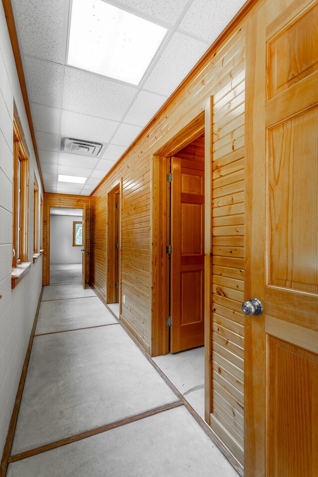 hallway with wooden walls and a drop ceiling